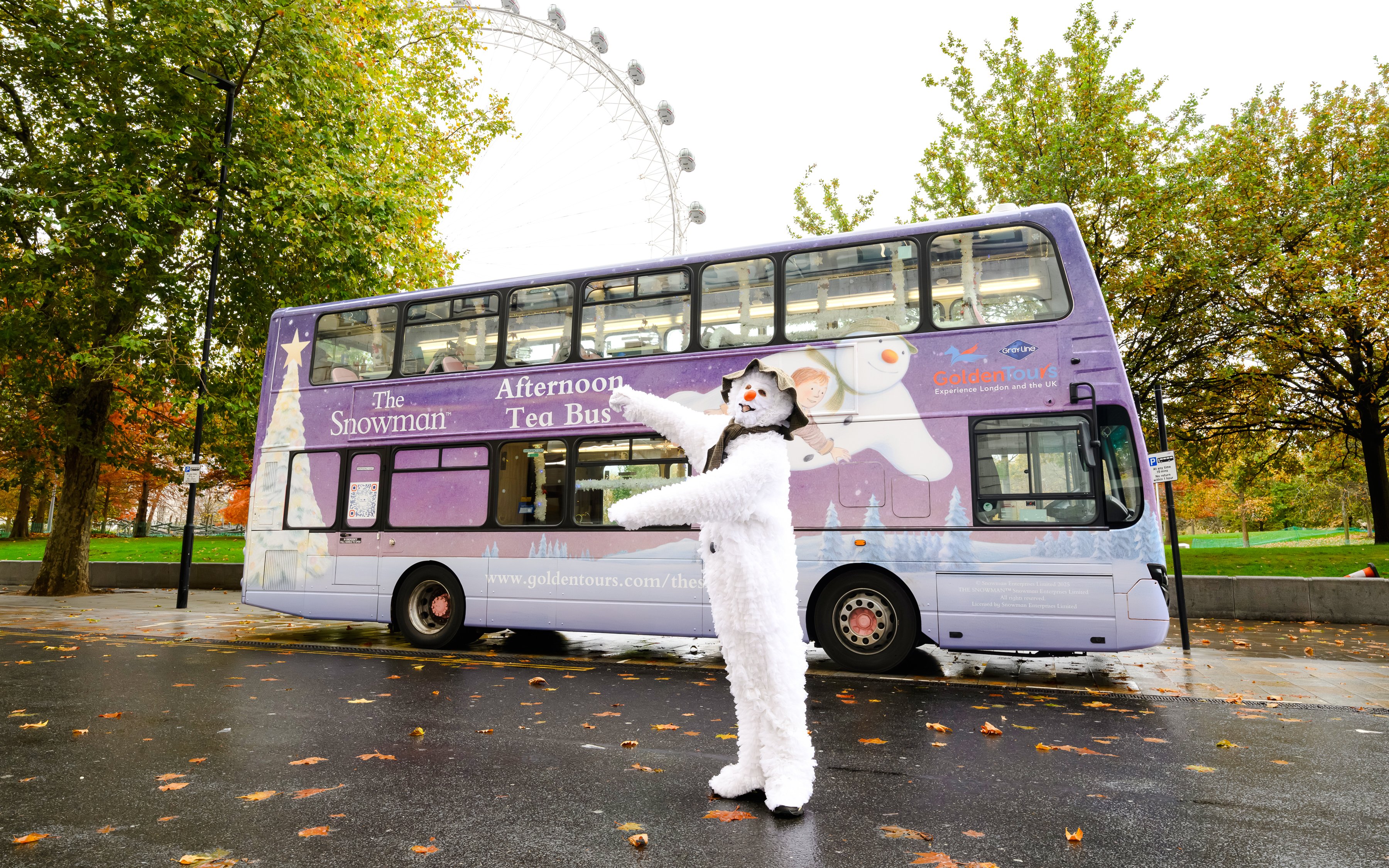 Snowman character in front of The Snowman™ Afternoon Tea Bus in London.