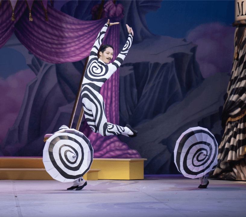 O Quebra-Nozes do ENB, uma bailarina num fato de corpo preto e branco rodado salta no centro do palco.